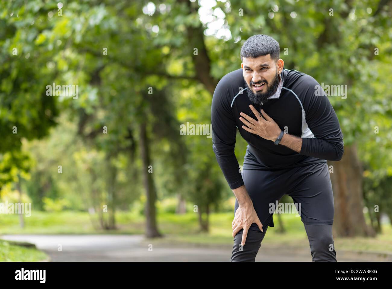 An exhausted male jogger resting with hands on knees in a green park