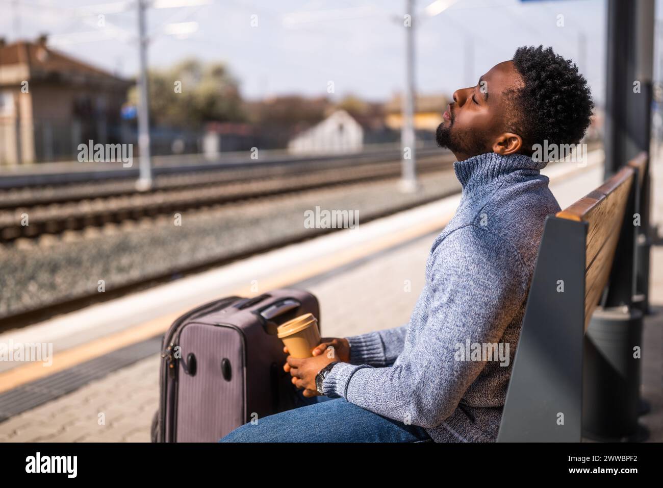 Tired man with a coffee sleeping on a bench at the railway station. Stock Photo