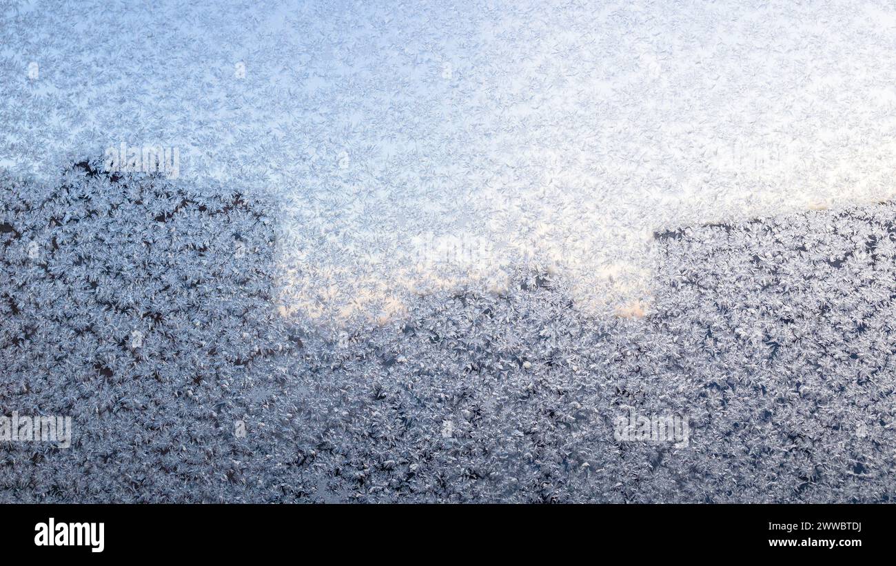 panoramic frosty pattern on window glass of residential apartment and silhouette of multi-storey city buildings in background on cold winter day Stock Photo