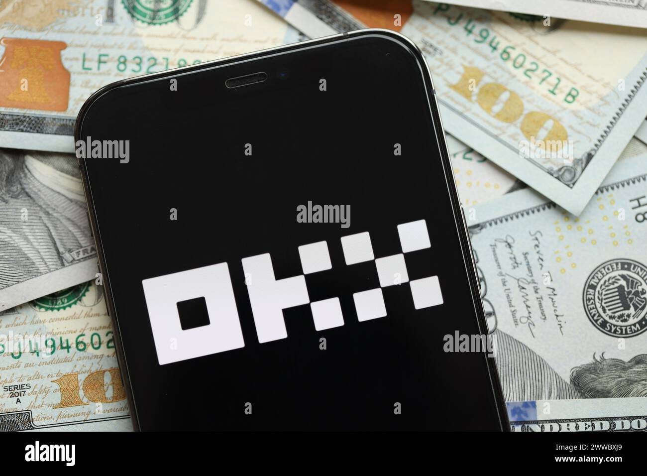 KYIV, UKRAINE - MARCH 15, 2024 OKX logo on iPhone display screen with many hundred dollar bills. Cryptocurrency exchange portal Stock Photo
