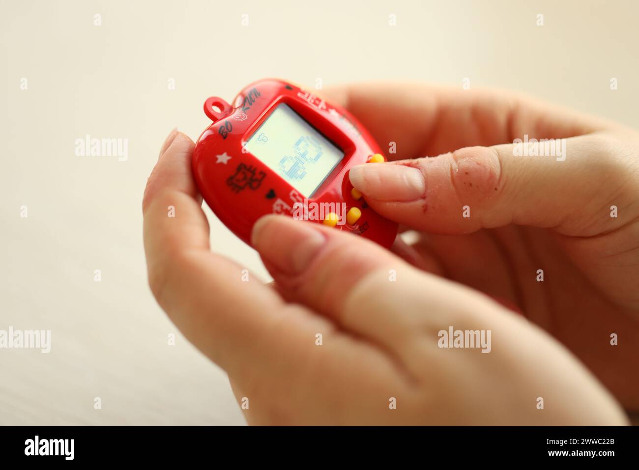 KYIV, UKRAINE - MARCH 9, 2024 Retro pet keychain game tamagotchi in red plastic case in female hands close up Stock Photo