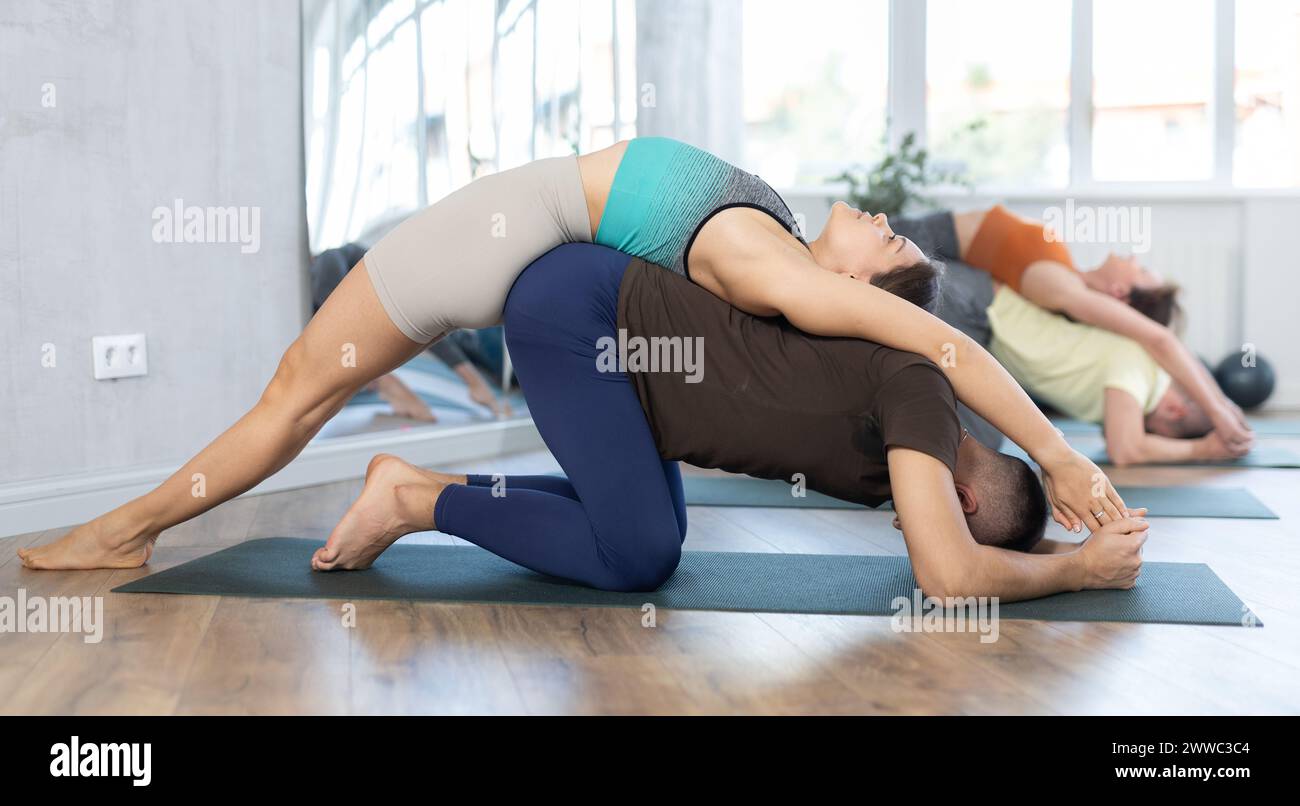 Young woman and man with flexible body doing gymnastics warm-up stretching exercises and acrobatic poses acro yoga during group classes at gym Stock Photo