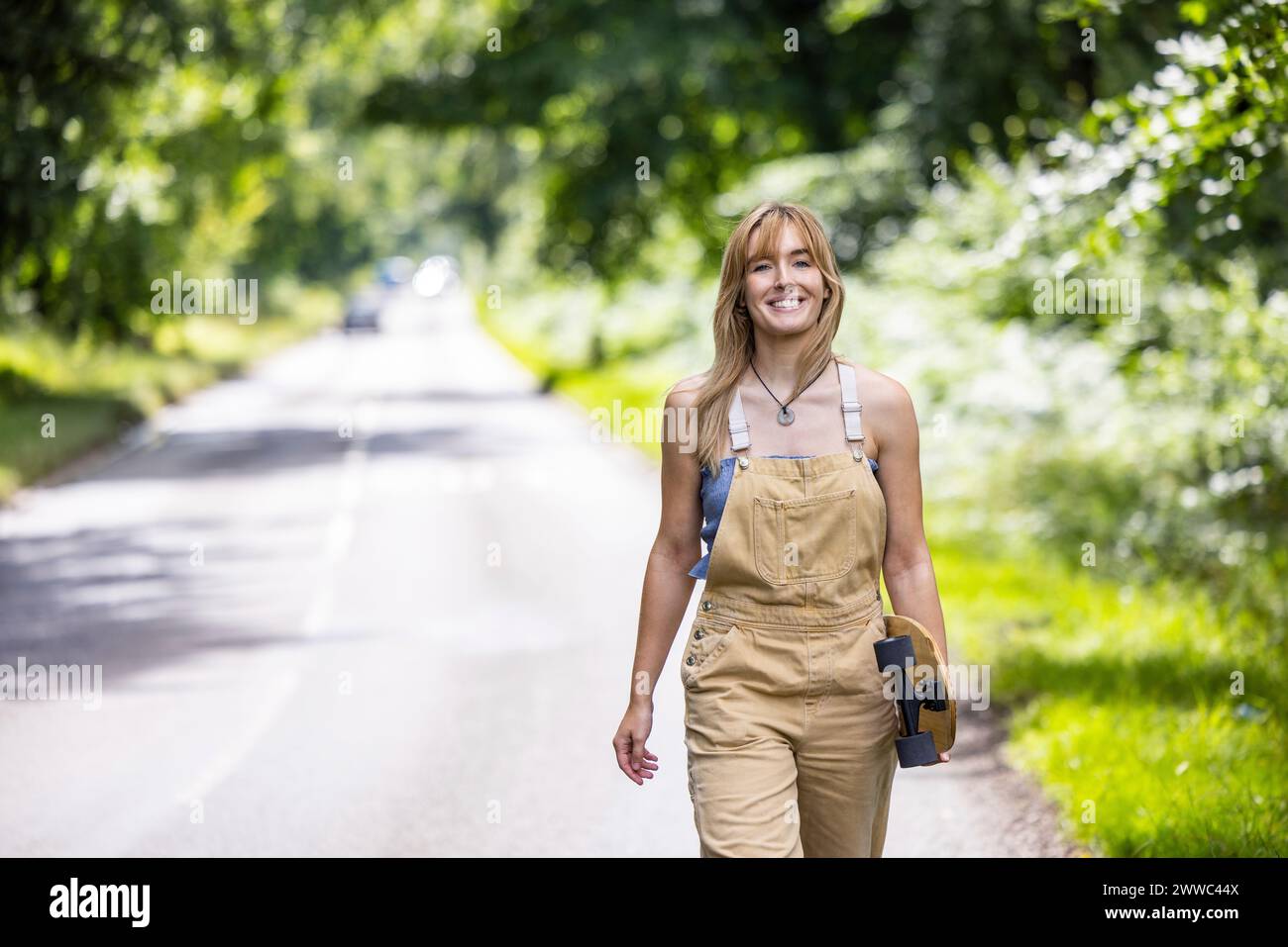 Happy woman walking with skateboard in forest Stock Photo