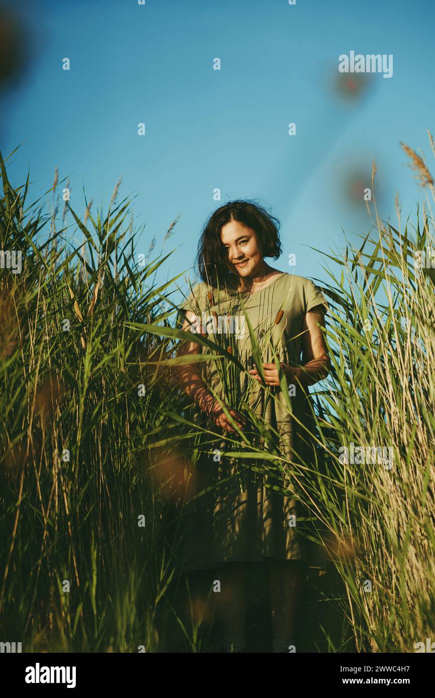 Mature woman standing amidst tall reeds in field on sunny day Stock Photo