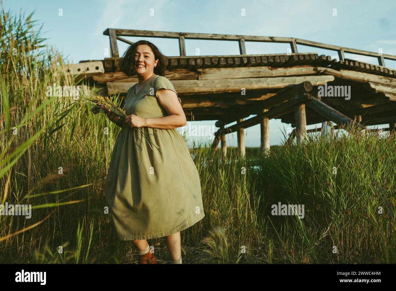 Smiling woman walking among reeds near bridge in field Stock Photo