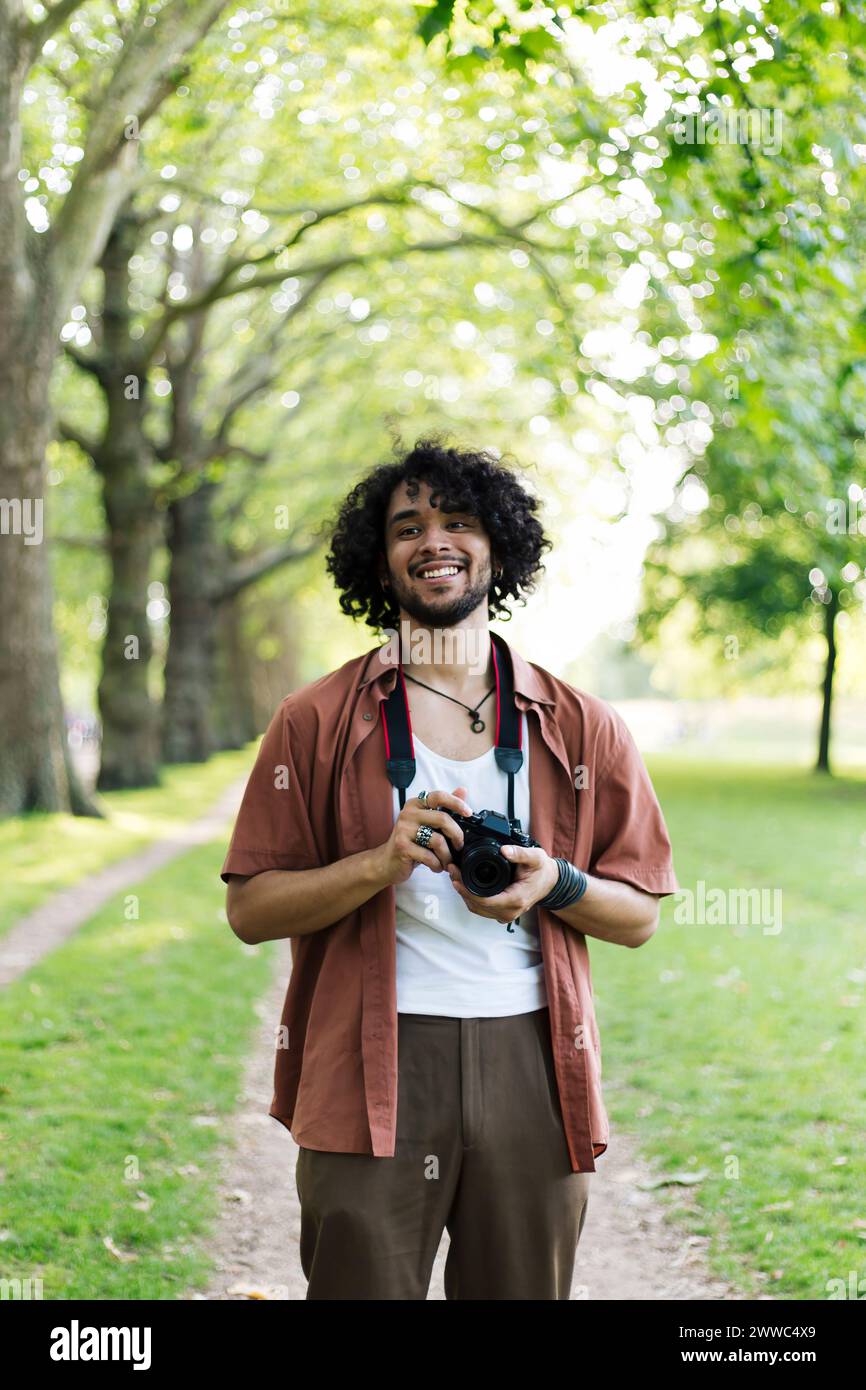 Smiling man holding camera and standing at park Stock Photo