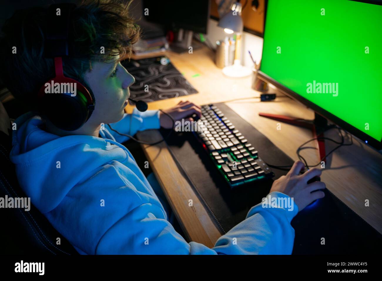 Boy wearing headset and playing video game on computer at home Stock Photo