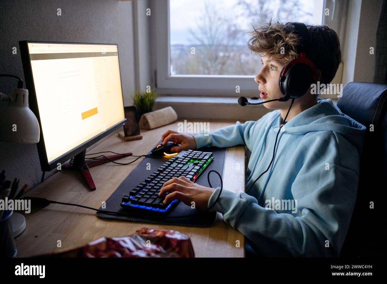 Boy wearing headset and playing video game on computer at desk Stock Photo