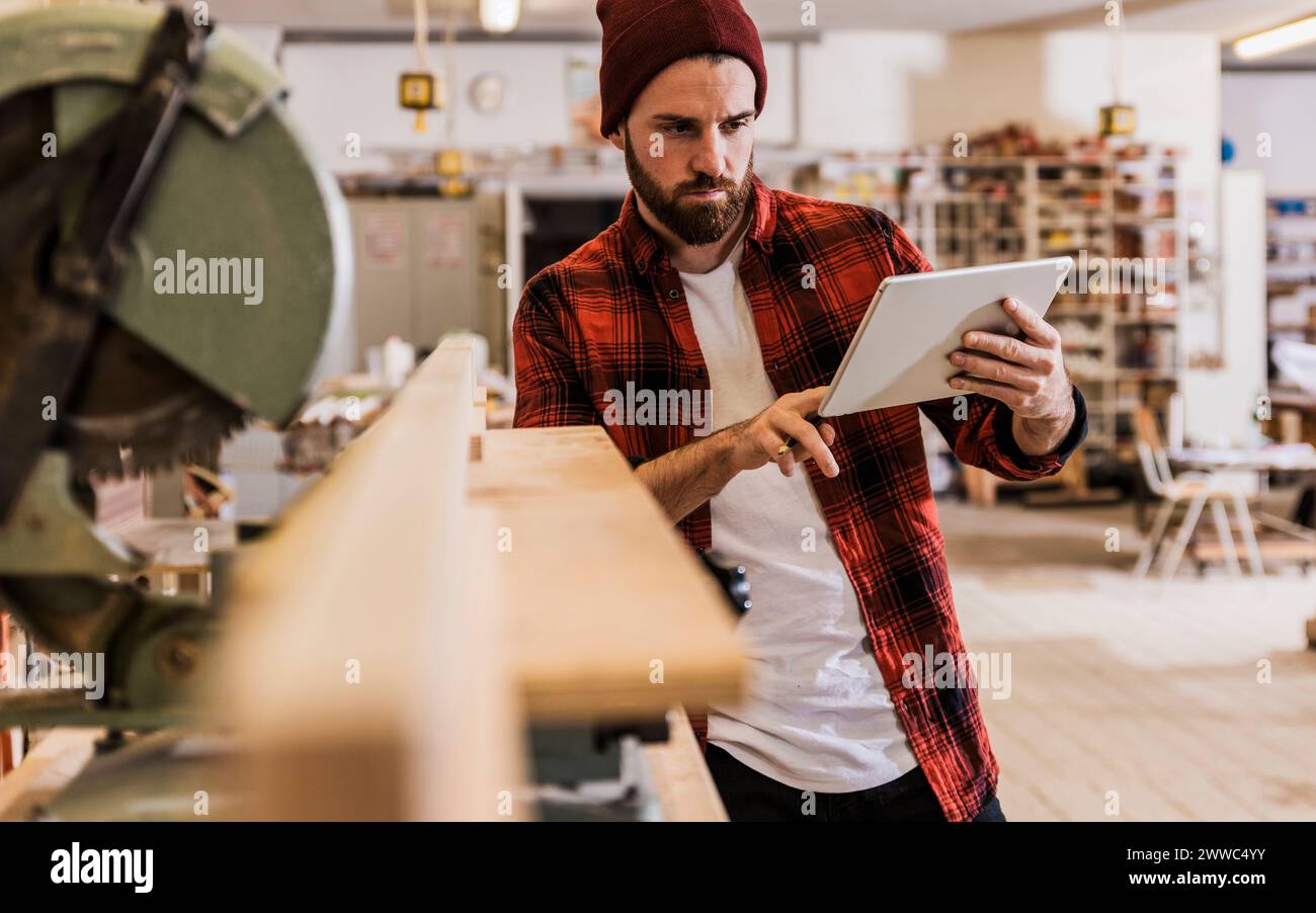 Young carpenter using tablet PC by machinery at workshop Stock Photo