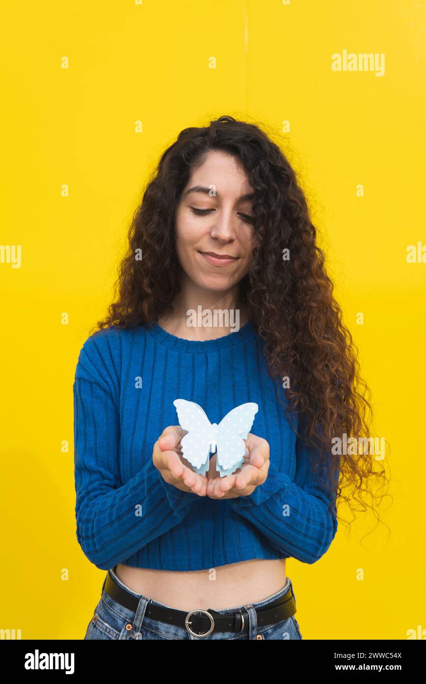 Woman holding butterfly in hands against yellow background Stock Photo