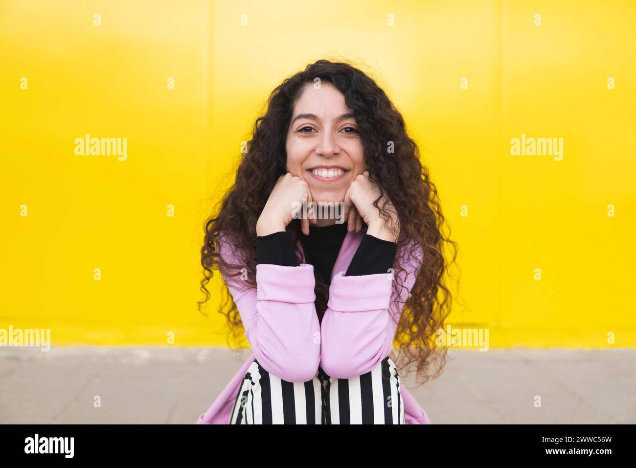 Happy woman sitting in front of yellow wall Stock Photo