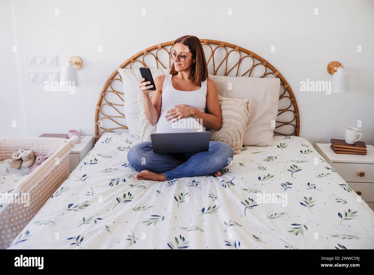 Pregnant freelancer using smart phone on bed at home office Stock Photo