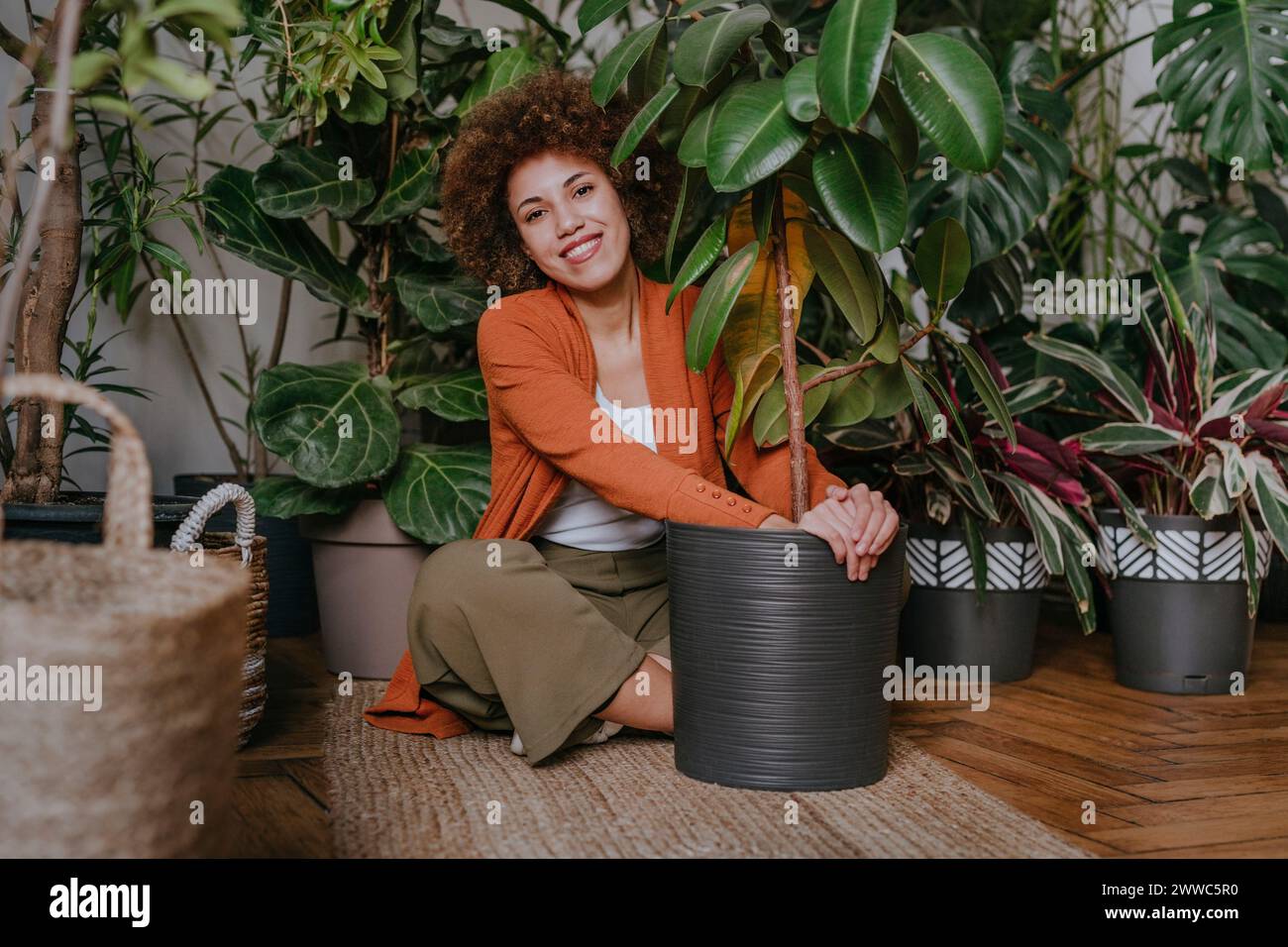 Smiling young woman sitting with plants on carpet Stock Photo
