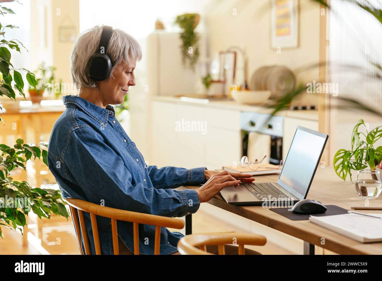 Smiling freelancer wearing wireless headphones and working on laptop at home office Stock Photo