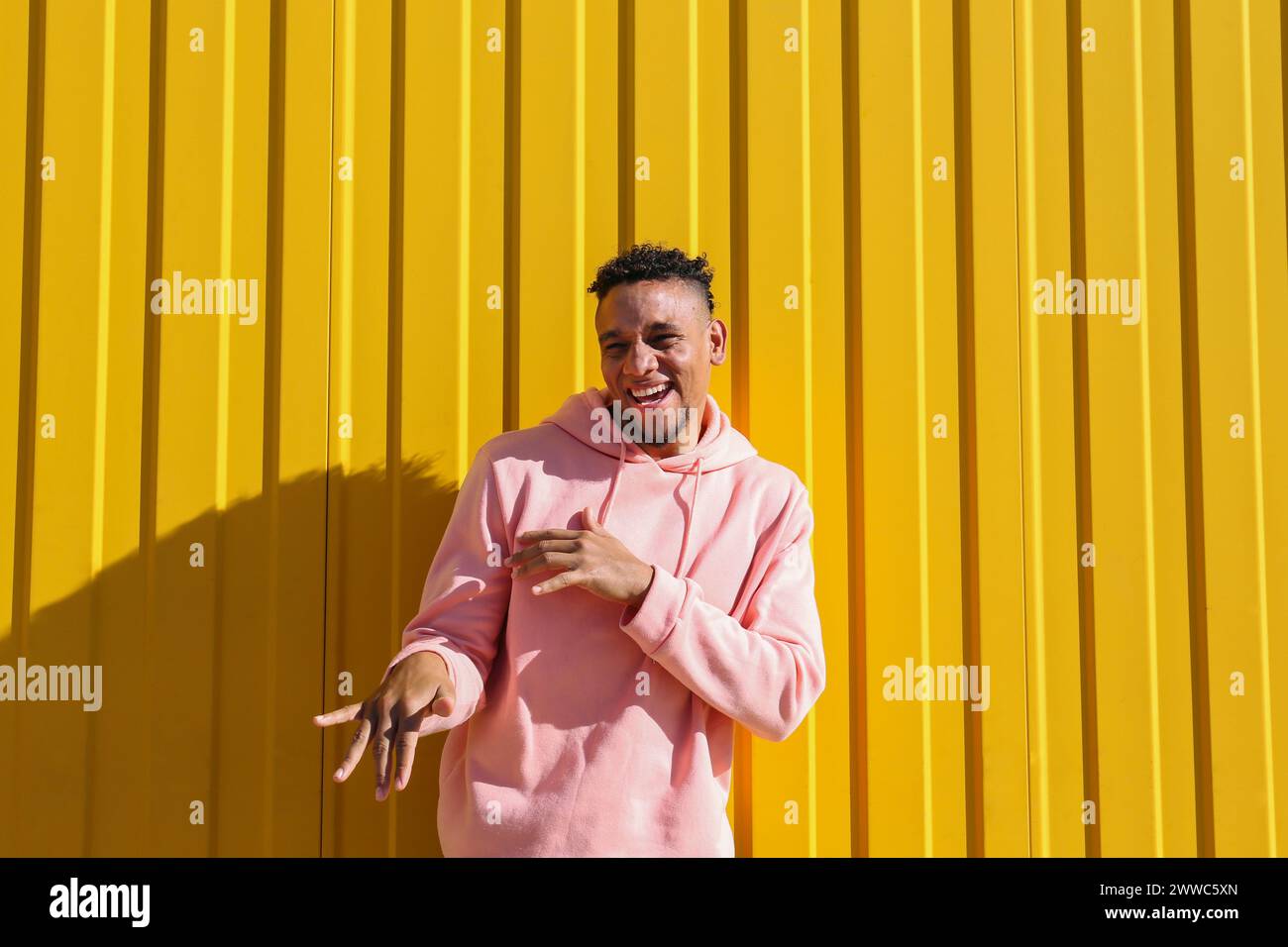 Cheerful young man having fun in front of yellow wall Stock Photo