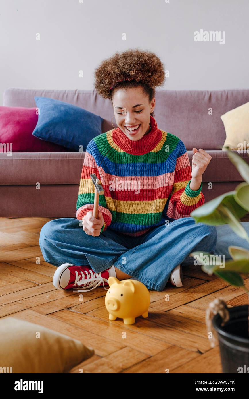 Happy young woman breaking piggy bank with hammer Stock Photo - Alamy