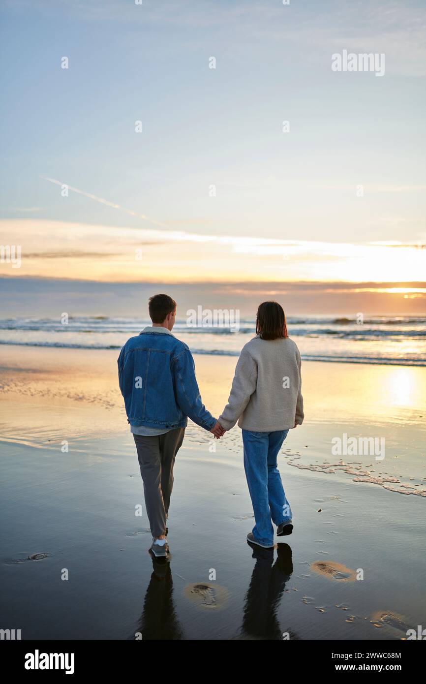 Young man and woman holding hands at coastline on beach Stock Photo - Alamy