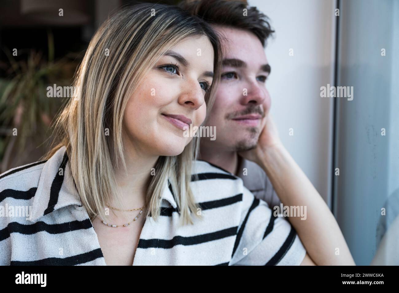 Smiling young couple looking through window at home Stock Photo