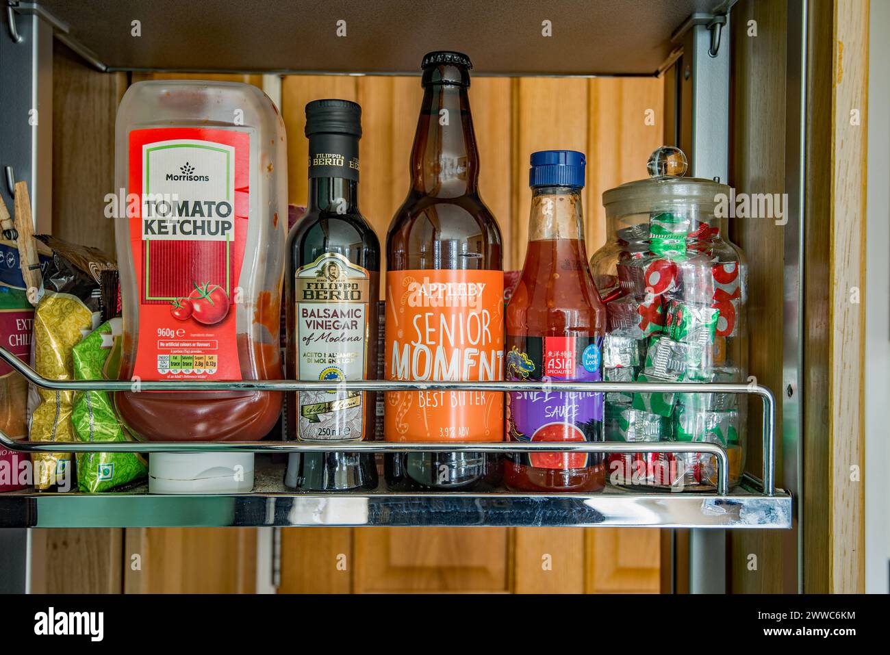 A Senior Moment in the kitchen with a misplaced bottle of beer on a shelf full of sauces etc Stock Photo