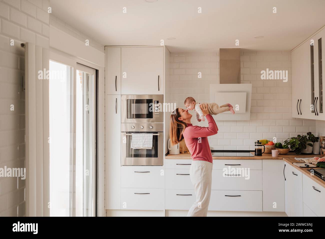 Smiling woman holding baby girl in kitchen at home Stock Photo