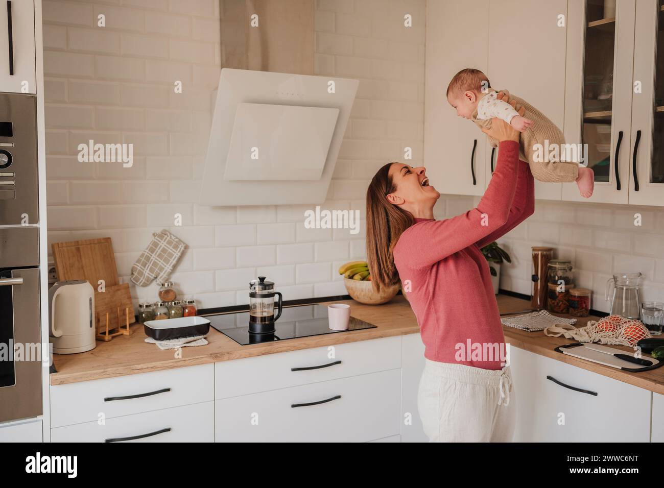Happy woman playing with baby girl in kitchen Stock Photo