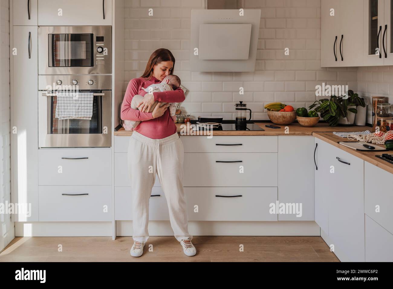 Woman embracing baby daughter in kitchen at home Stock Photo