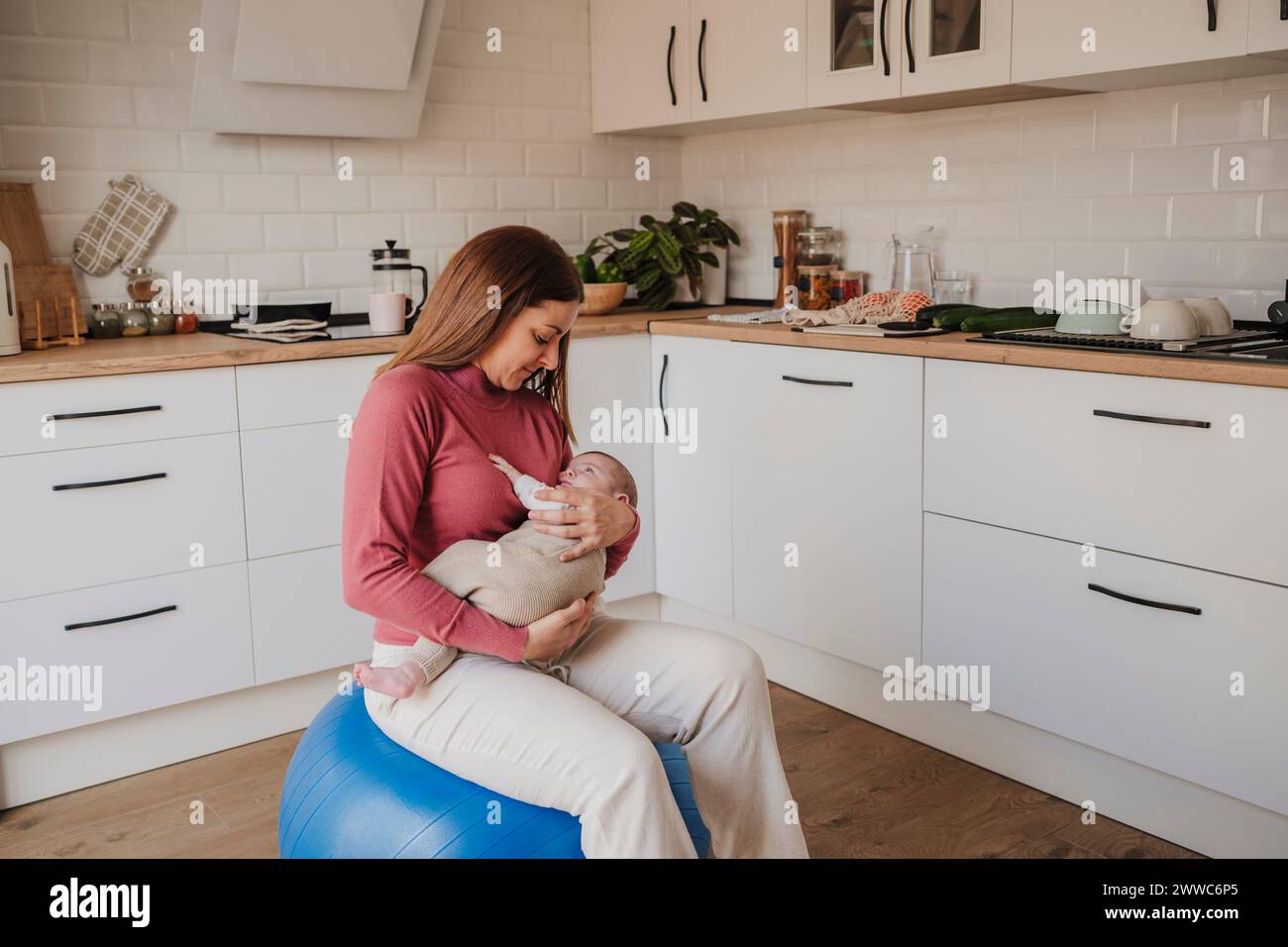 Mother holding baby daughter and sitting on fitness ball Stock Photo