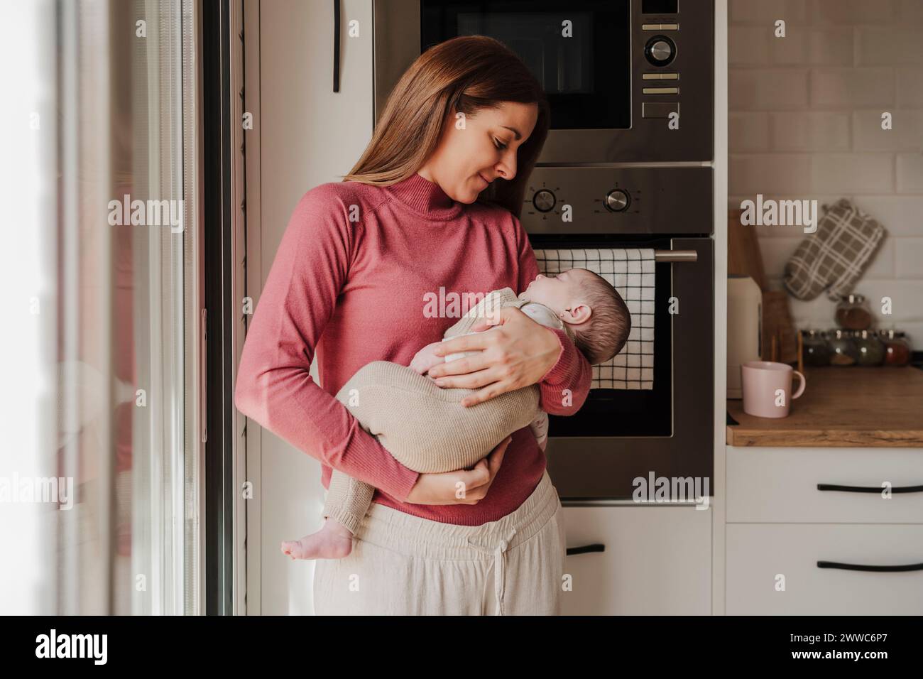 Smiling woman holding baby daughter in kitchen Stock Photo