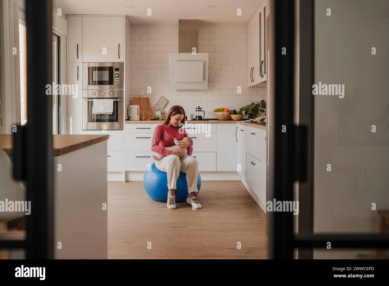 Woman sitting with baby daughter on fitness ball at home Stock Photo