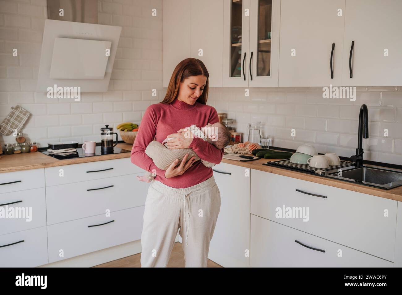 Smiling woman standing with baby daughter in kitchen Stock Photo