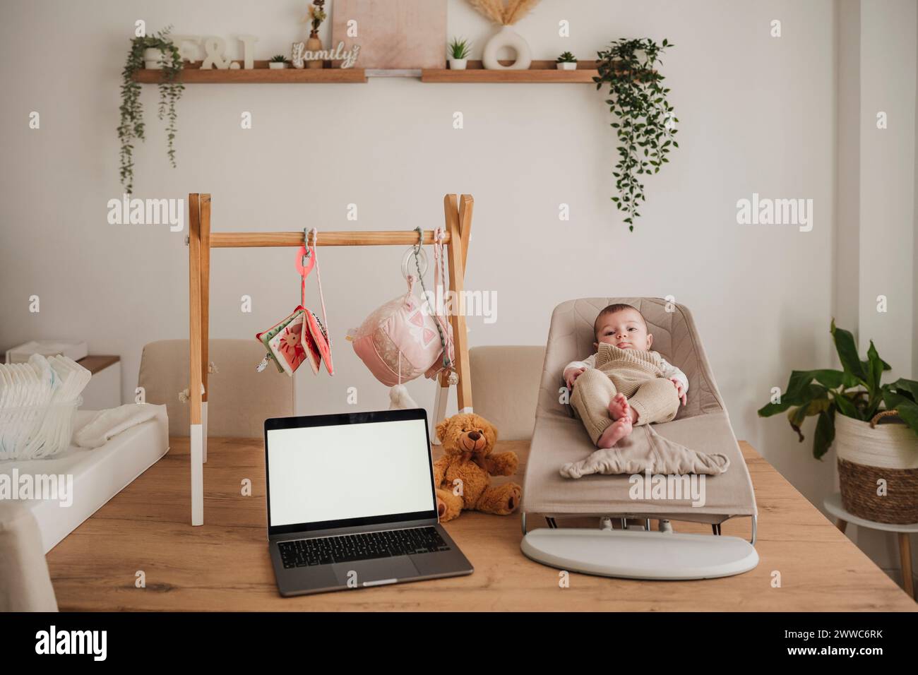 Baby girl sitting on bouncer chair near laptop at home Stock Photo