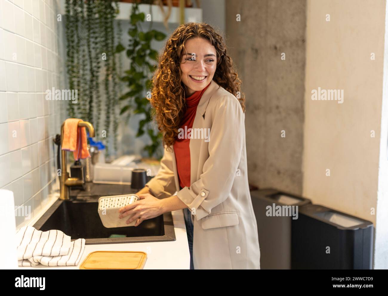 Smiling businesswoman washing container at sink in office Stock Photo