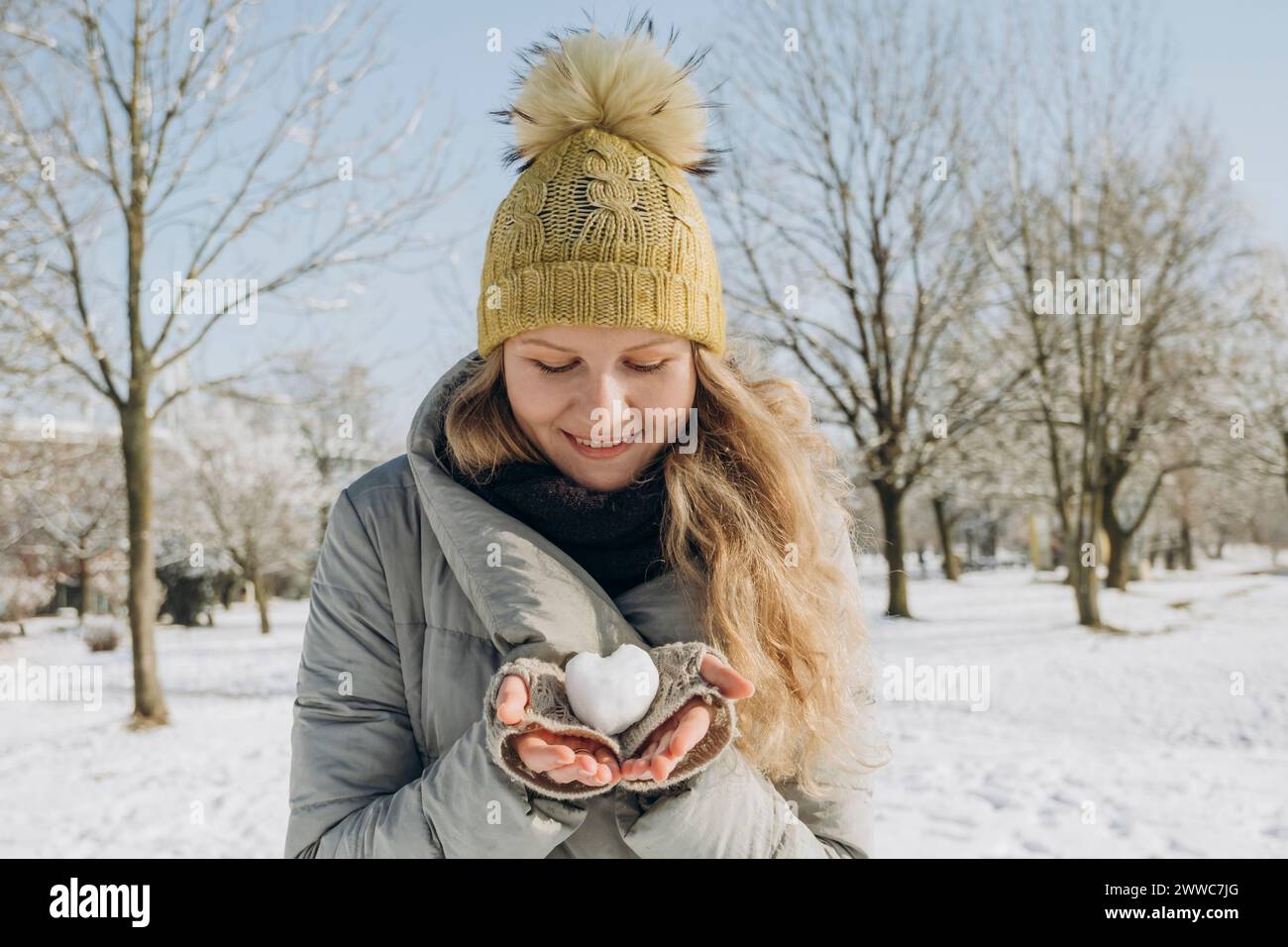 Smiling woman holding heart shaped snowball in hand Stock Photo