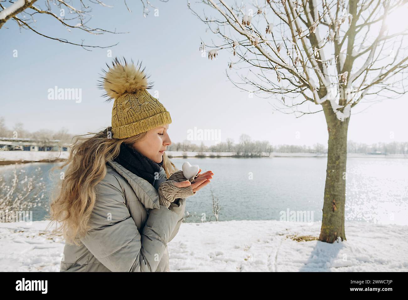 Woman with heart shaped snowball in hand near lake Stock Photo