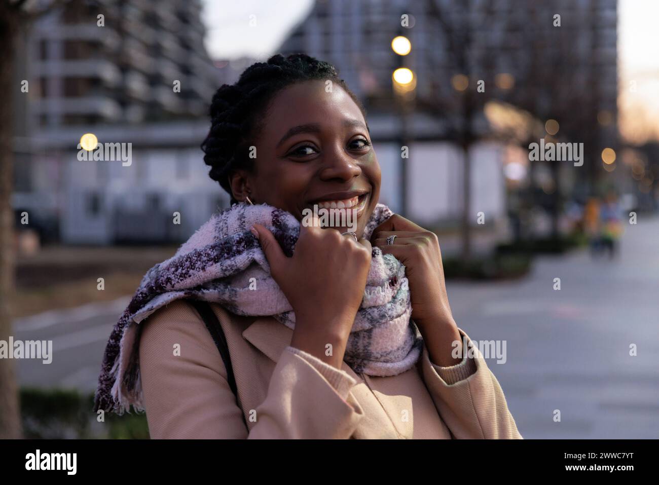 Happy woman wearing scarf in city at dusk Stock Photo