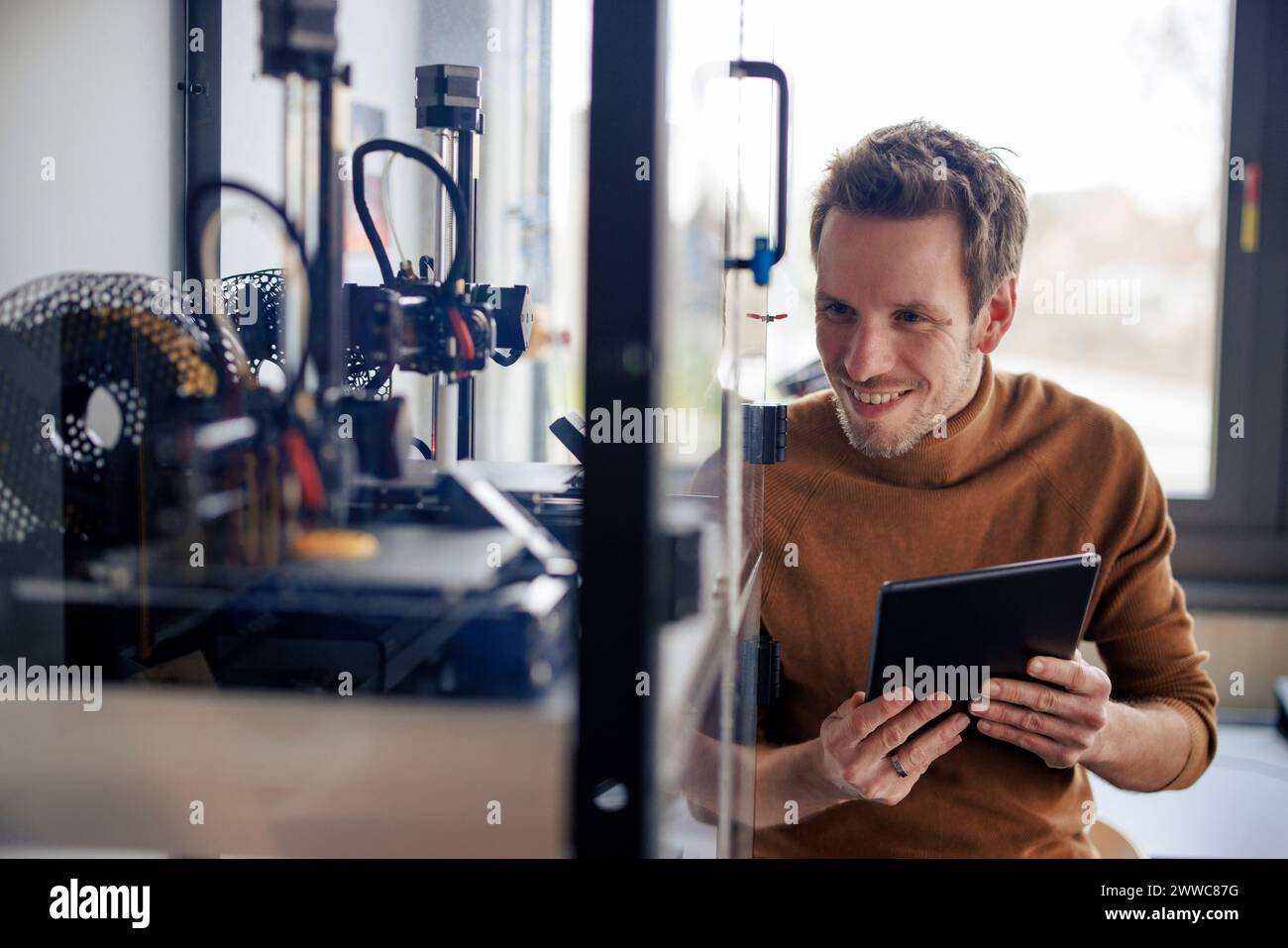 Smiling engineer holding tablet PC and looking at 3d printer in workshop Stock Photo