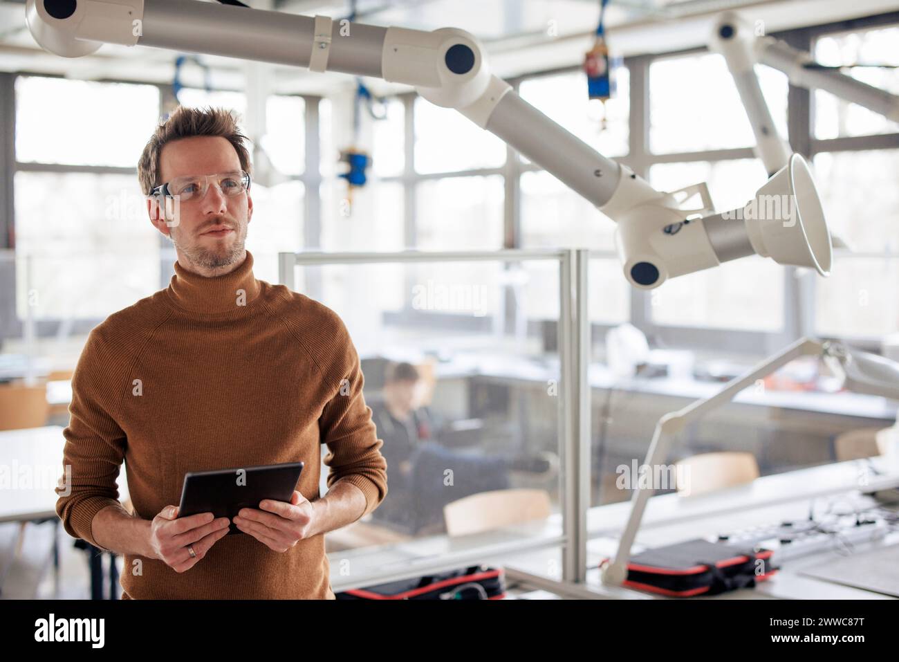 Thoughtful engineer holding tablet PC by extraction arm at workshop Stock Photo