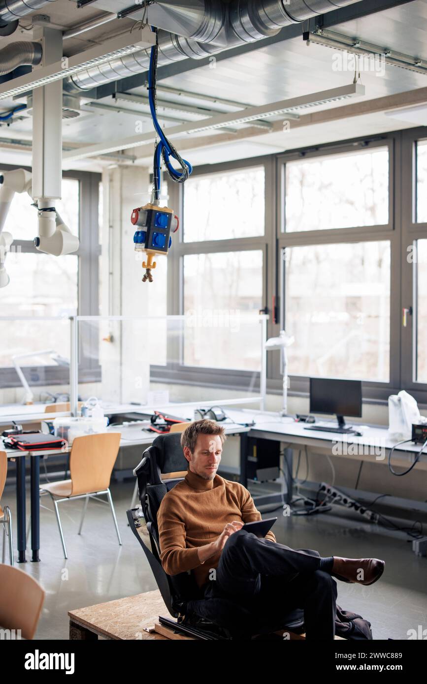 Mature engineer using tablet PC sitting on chair at workshop Stock Photo