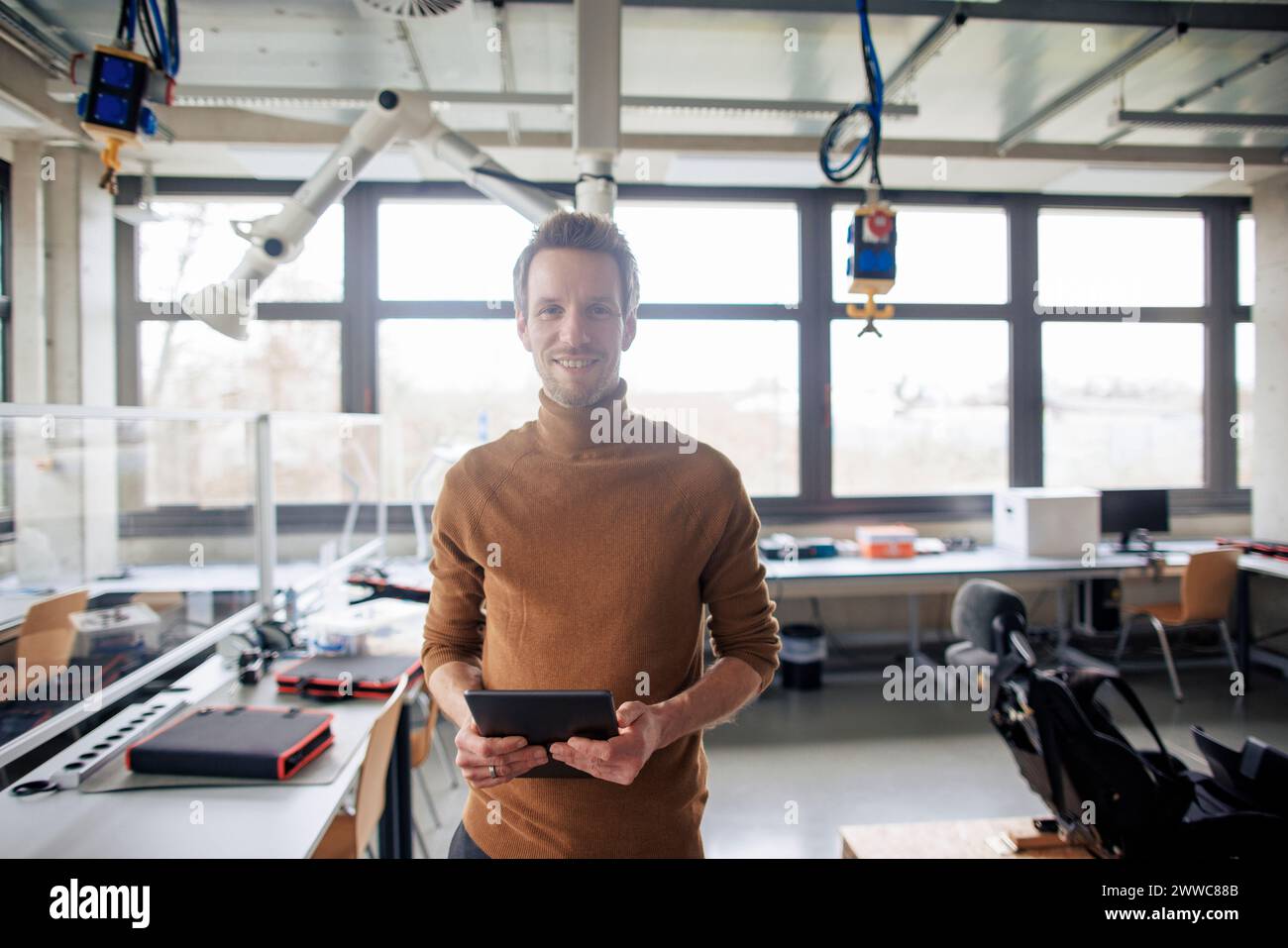 Smiling engineer holding tablet and standing at workshop Stock Photo