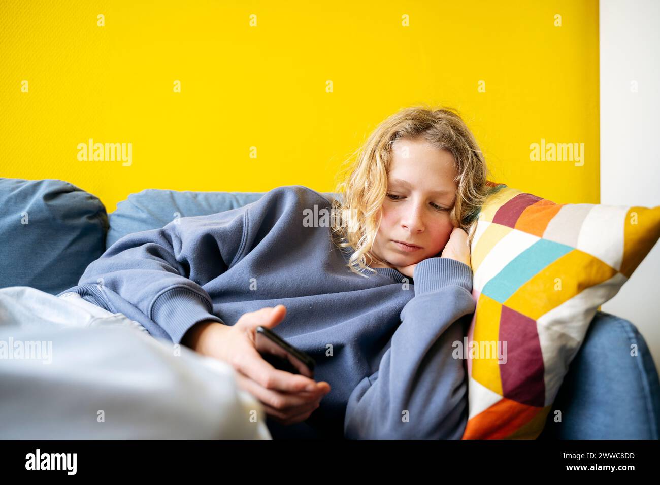 Boy lying on sofa and using smart phone at home Stock Photo