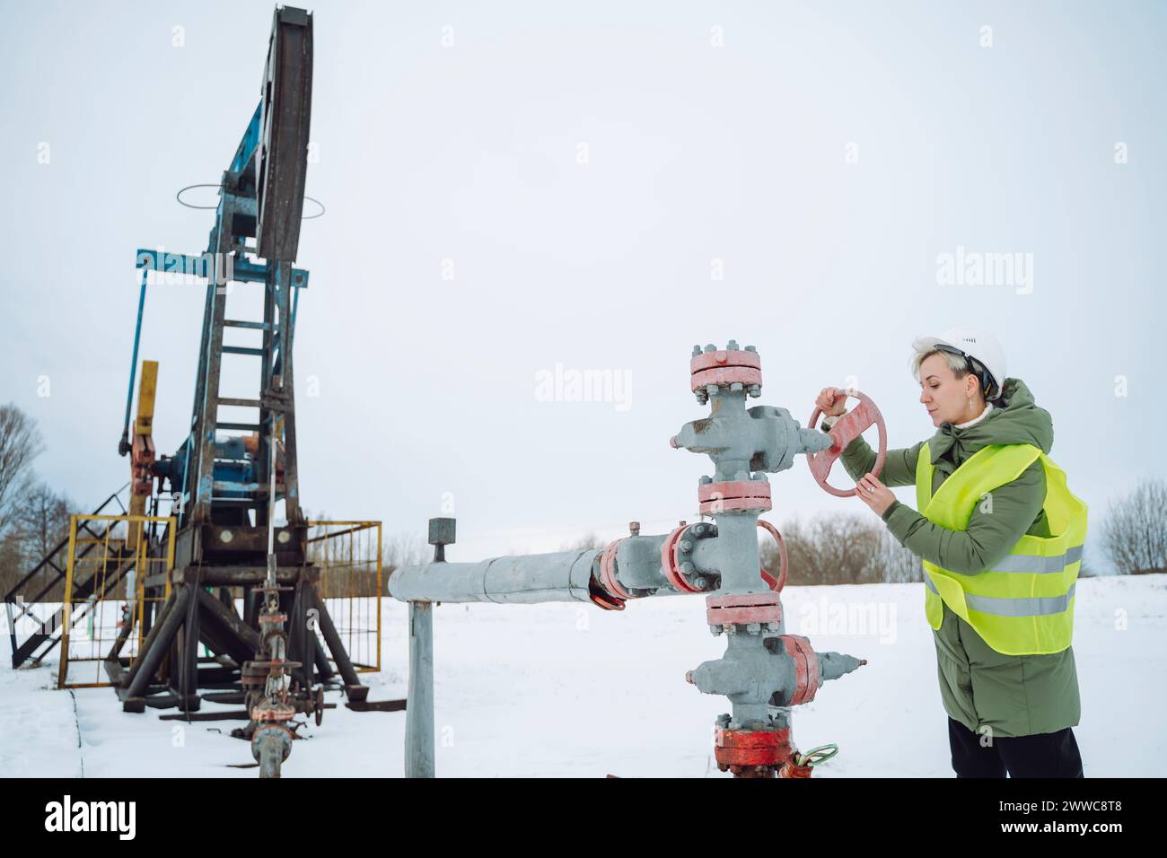 Engineer operating wellhead near drilling tower at oil field in winter Stock Photo