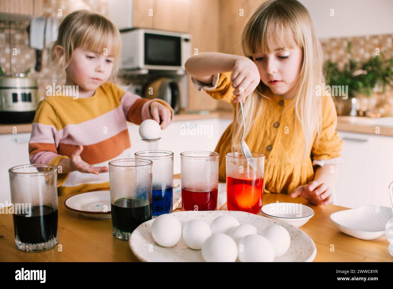 Sisters dipping Easter eggs in colored dye at home Stock Photo