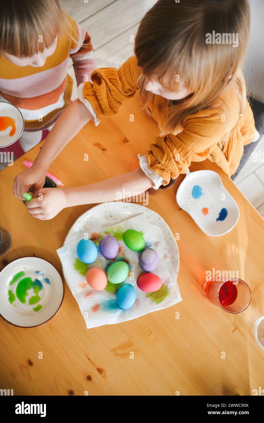 Girls coloring Easter eggs on table at home Stock Photo