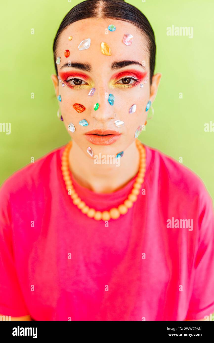 Young woman with gem stickers on face against green background Stock Photo