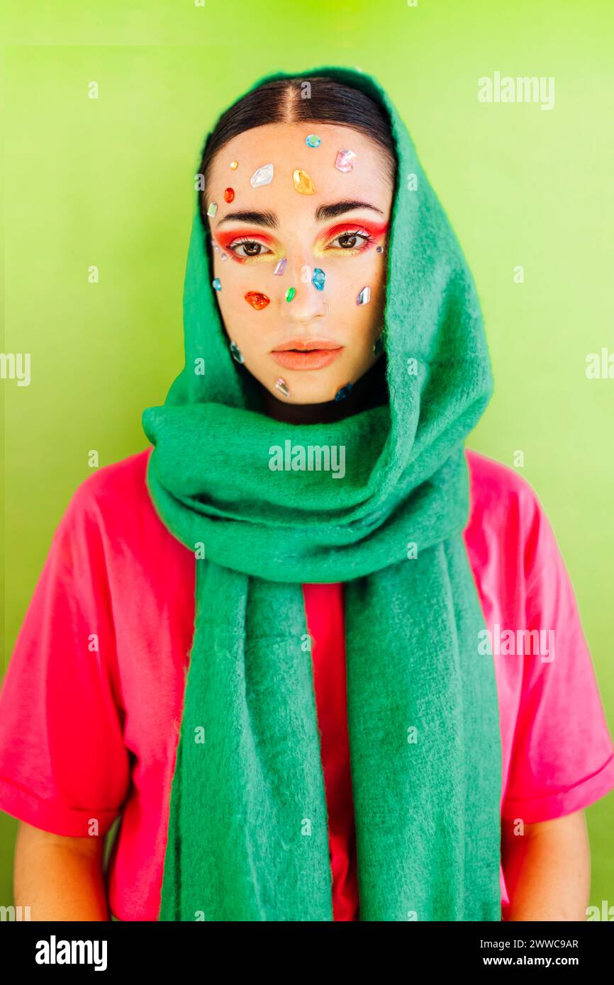 Woman with gem stickers on face wearing green scarf against green background Stock Photo