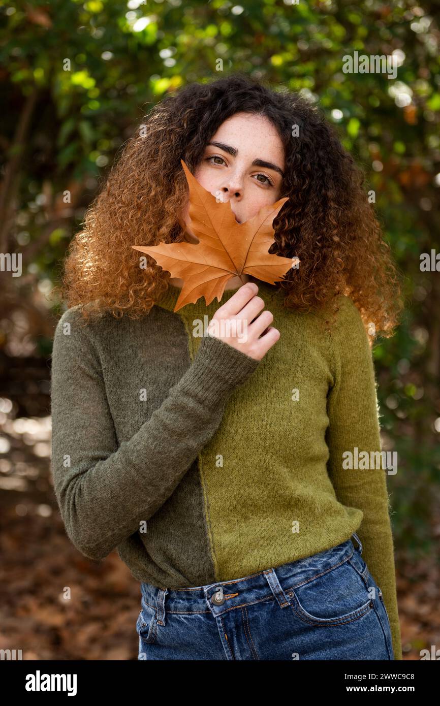 Young woman covering mouth with maple leaf at park Stock Photo - Alamy