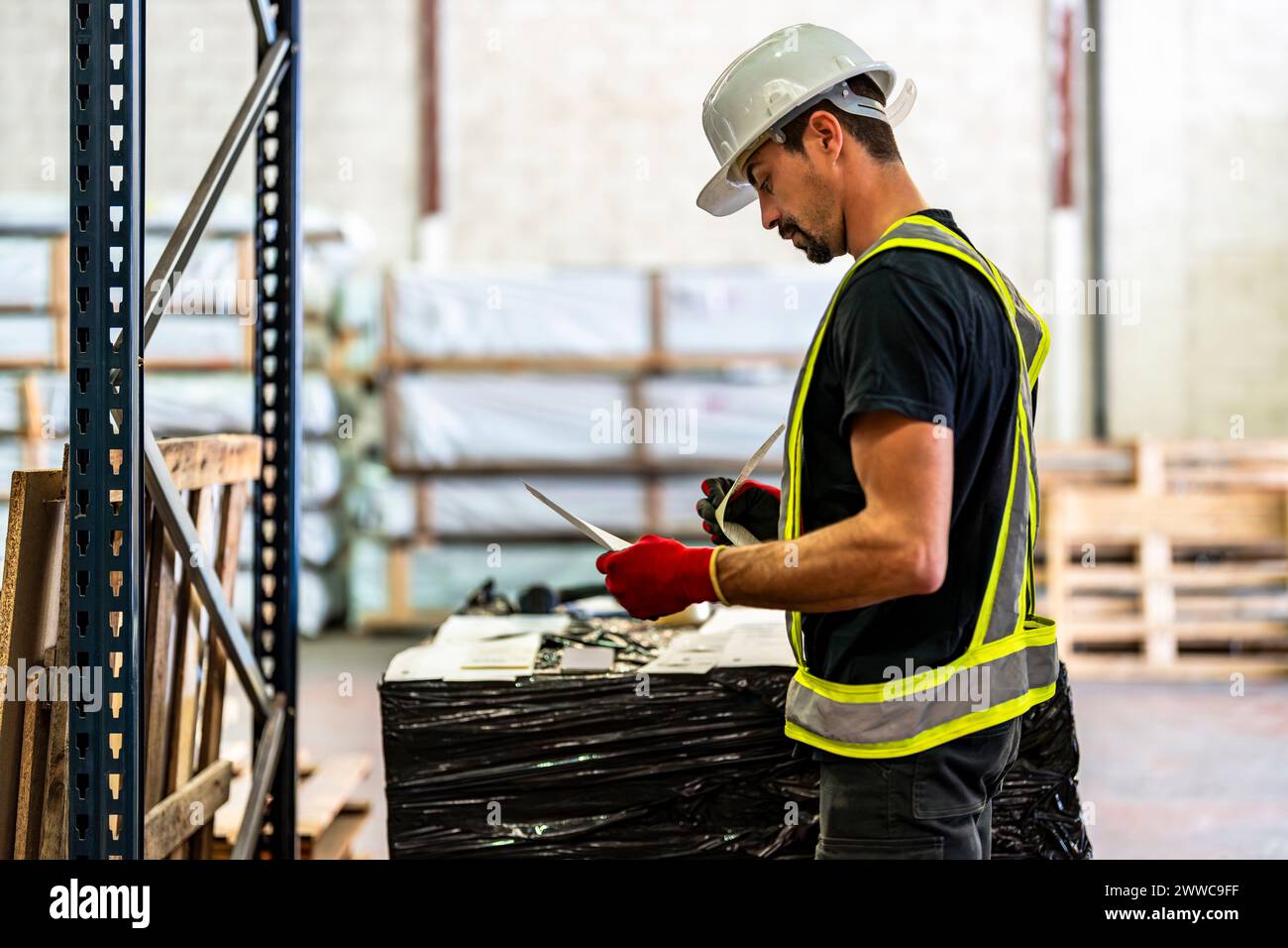 Worker wearing hardhat and examining documents at warehouse Stock Photo