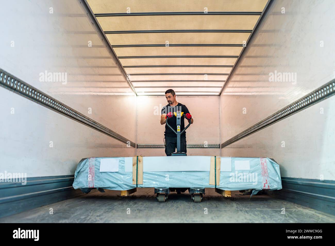 Worker pushing pallet jack loading in cargo container Stock Photo