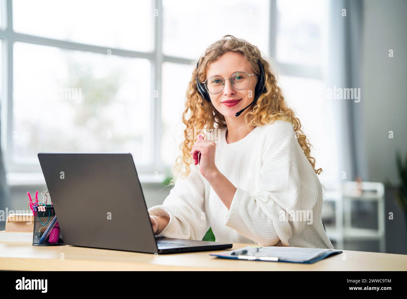 Smiling saleswoman wearing headset near laptop in office Stock Photo