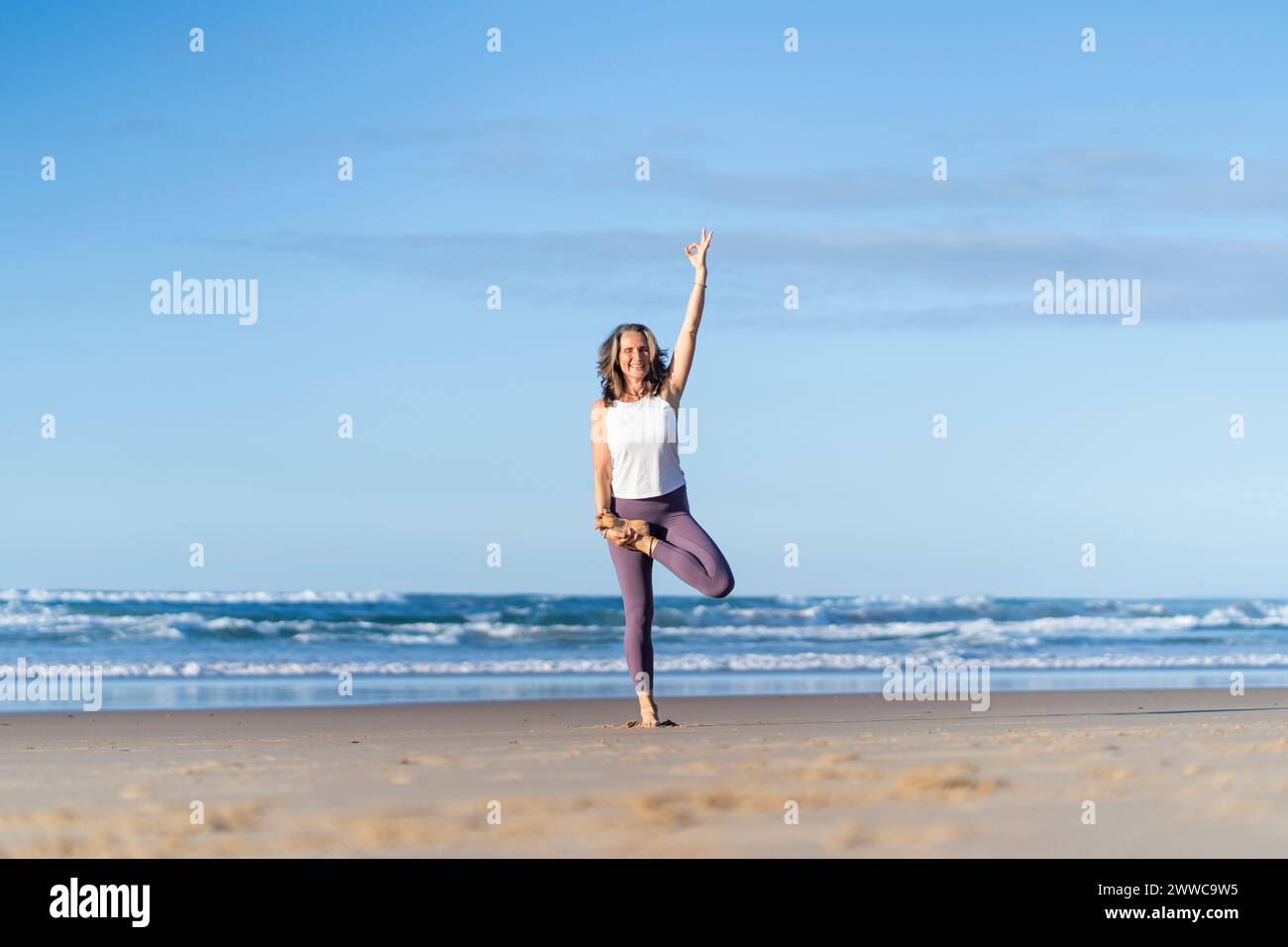 Mature woman doing tree yoga pose with hand raised at beach Stock Photo ...